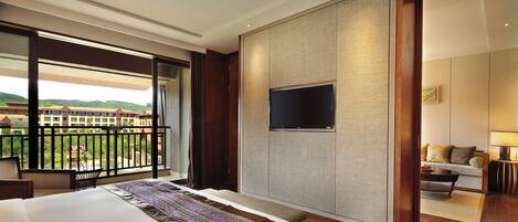 A hotel room with a large bed, a TV mounted on the wall, a balcony with a view, and a seating area with a sofa and coffee table.