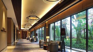 A hotel lobby with a long corridor, large windows, and modern chandeliers.