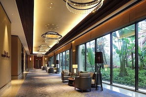 A hotel lobby with a long corridor, large windows, and modern chandeliers. - Crowne Plaza Resort Xishuangbanna Parkview by IHG (Xishuangbanna Dai)