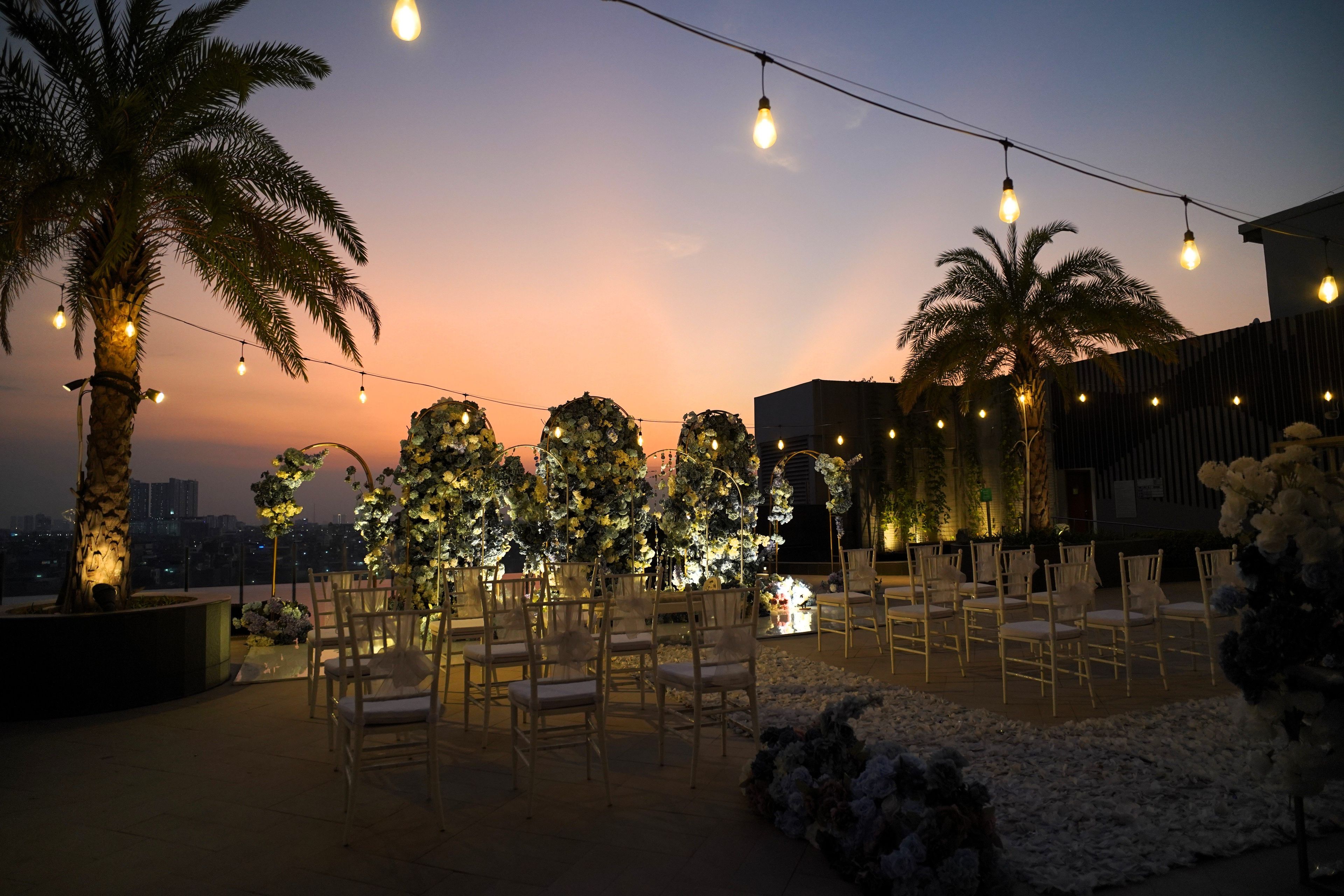 Un área de estar al aire libre con sillas y mesas, decorada con guirnaldas de luces y arreglos florales.
