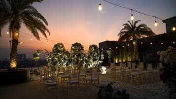 Un área de estar al aire libre con sillas y mesas, decorada con guirnaldas de luces y arreglos florales.