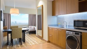 Une chambre d’hôtel comprenant un coin repas, un canapé, une grande fenêtre donnant sur la ville, une cuisine équipée d’un four à micro-ondes, d’un four traditionnel et d’un lave-linge.