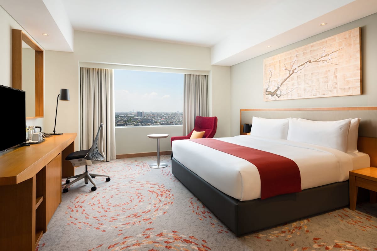 Hotelkamer met een groot bed, een bureau met een televisie, een stoel, een kleine tafel en uitzicht op de stad door het raam.