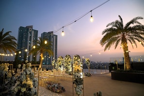 Un espacio para eventos al aire libre con luces colgantes, arreglos florales y asientos.
