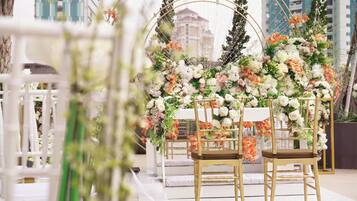 Un espacio interior con un arco floral, sillas blancas y una mesa blanca.