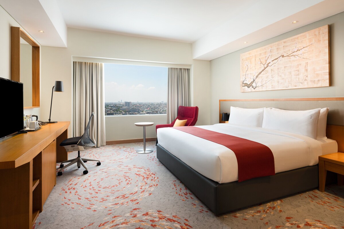 Une chambre d’hôtel avec un grand lit, un bureau avec une télévision, une chaise, une petite table et une vue sur la ville.