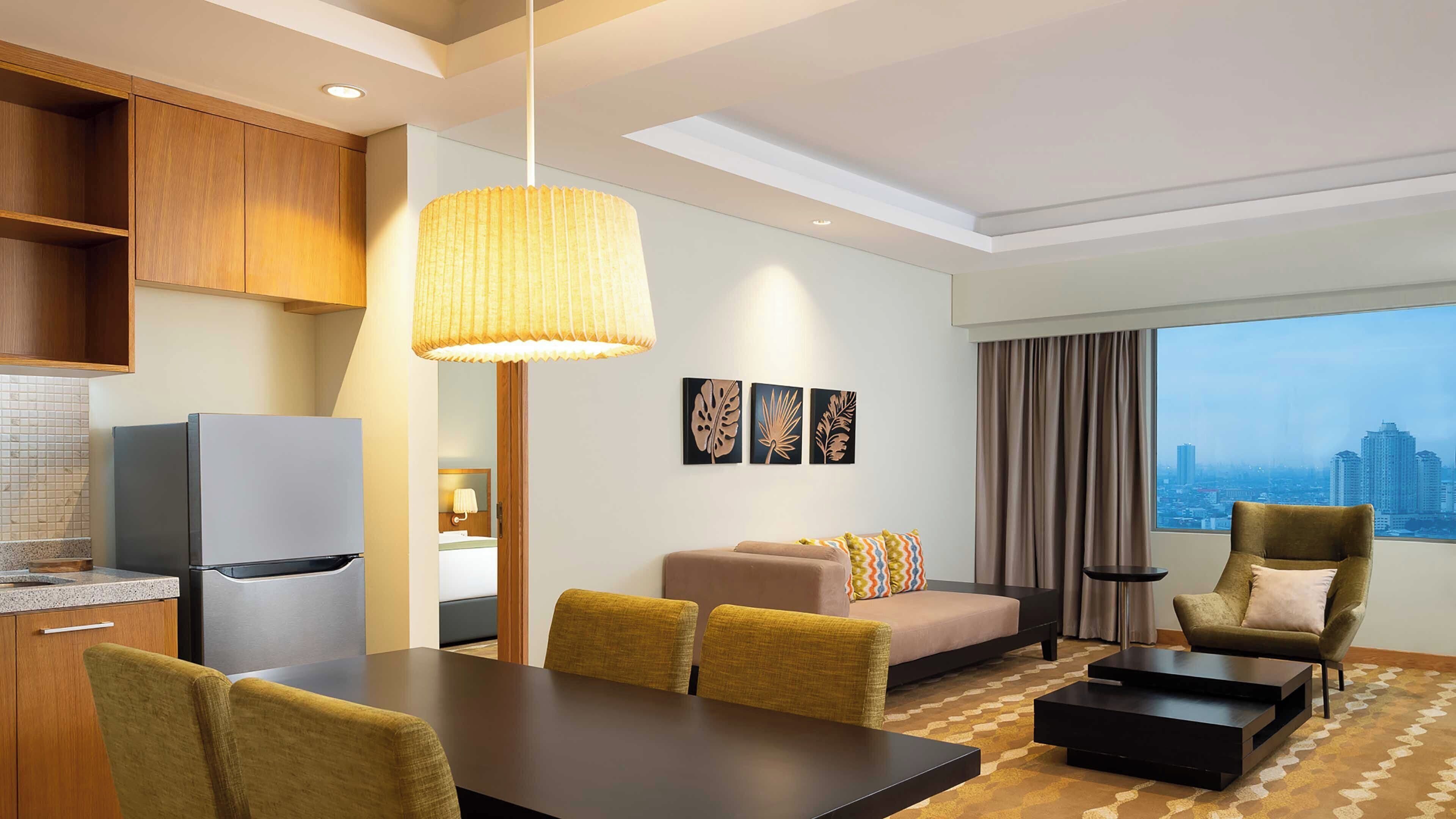 A hotel room with a dining area, a sofa, a coffee table, a TV, and a city view.