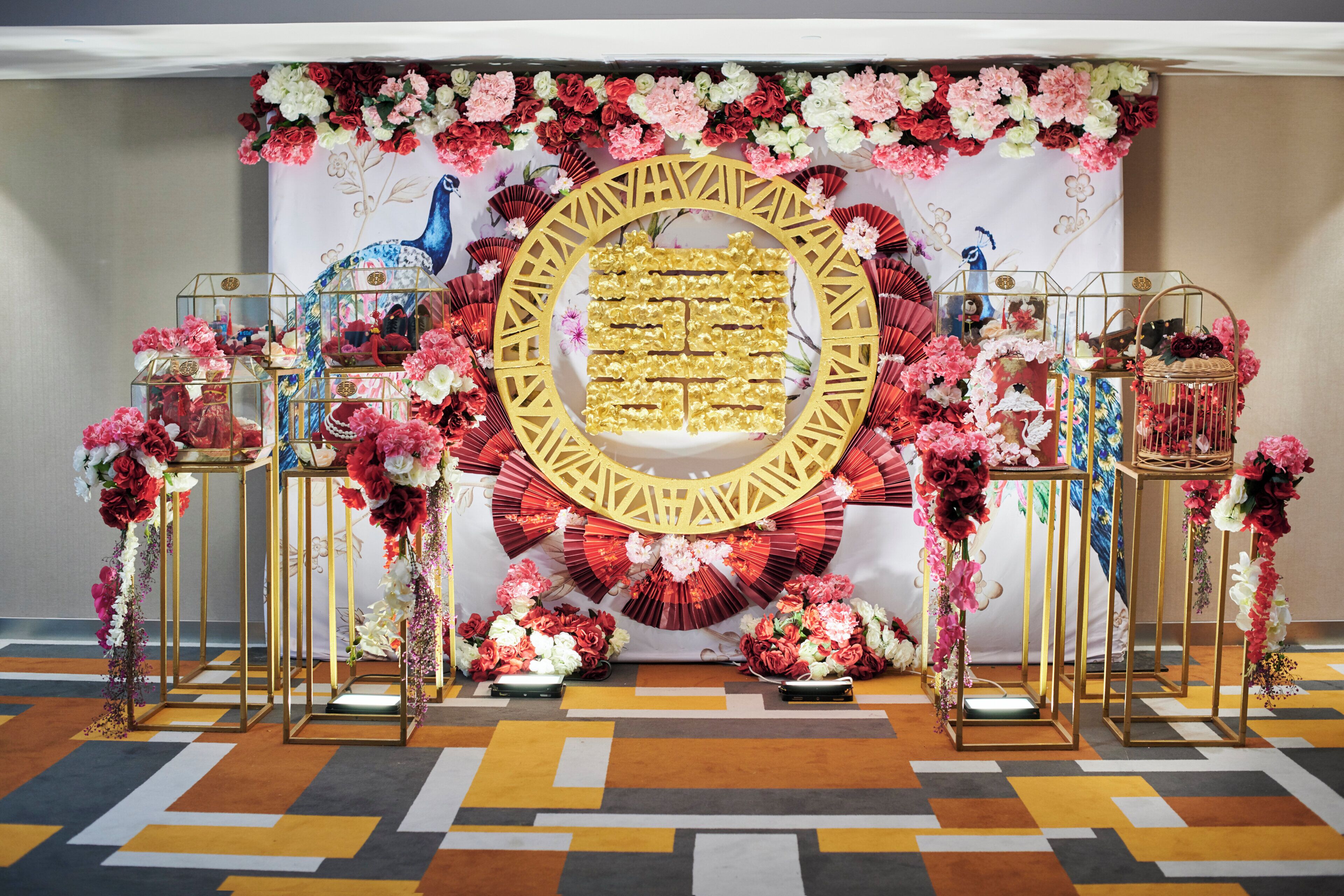 A decorated event space with floral arrangements, a central golden emblem, and glass display cases.