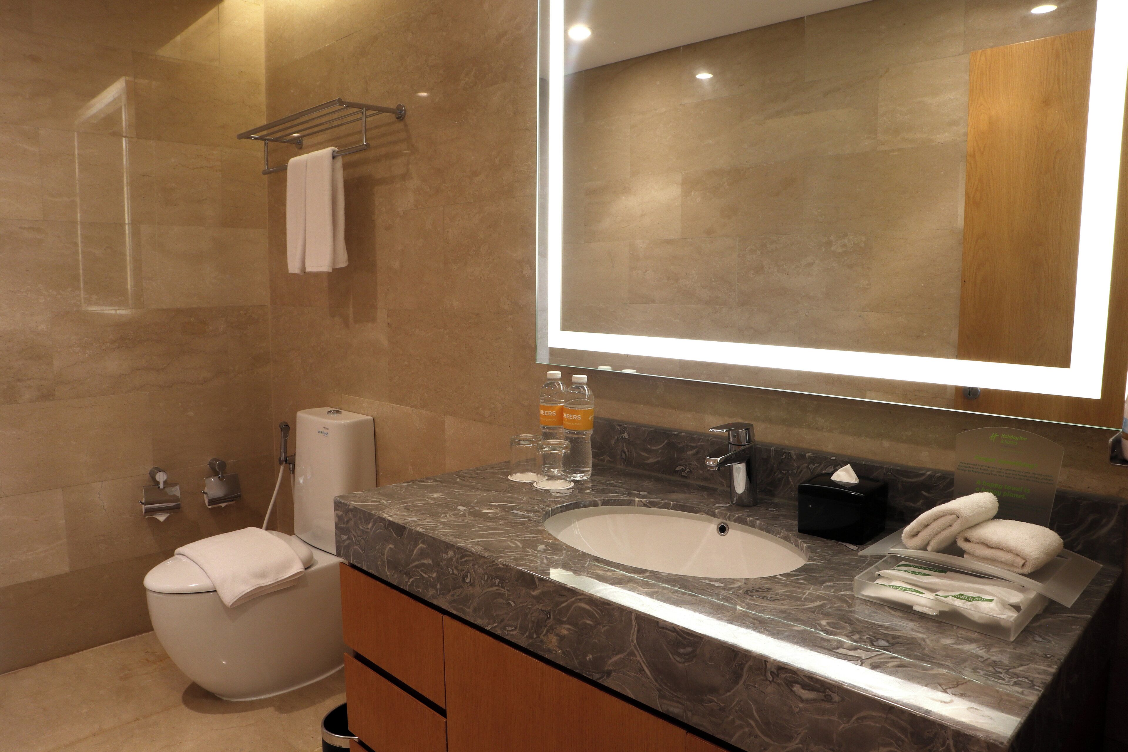 Une salle de bain moderne avec un lavabo en marbre, un grand miroir, un porte-serviettes et des toilettes.