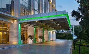 Una entrada de hotel moderna con un vestíbulo cubierto, puertas de vidrio y plantas en macetas.