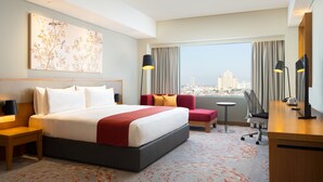 Habitación de hotel con una cama grande, un escritorio, una silla y vista a un paisaje urbano.