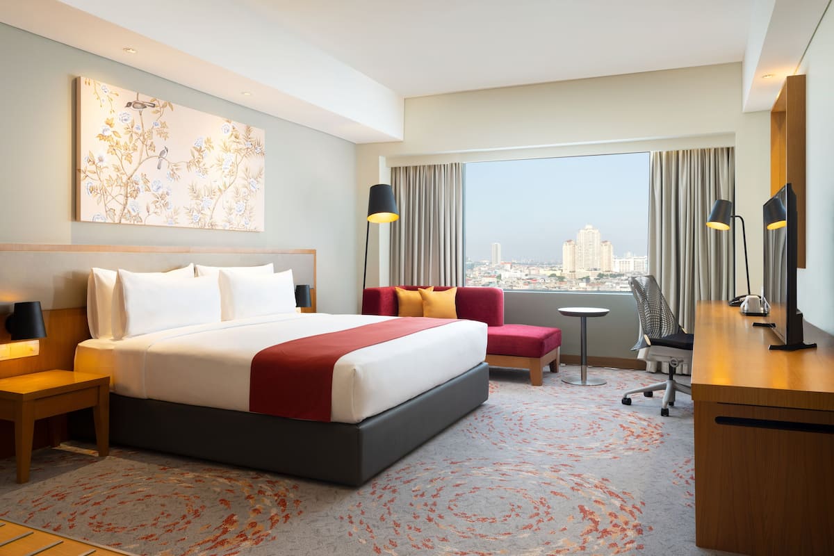 Een hotelkamer met een groot bed, een bureau, een stoel en uitzicht op een stadsgezicht.