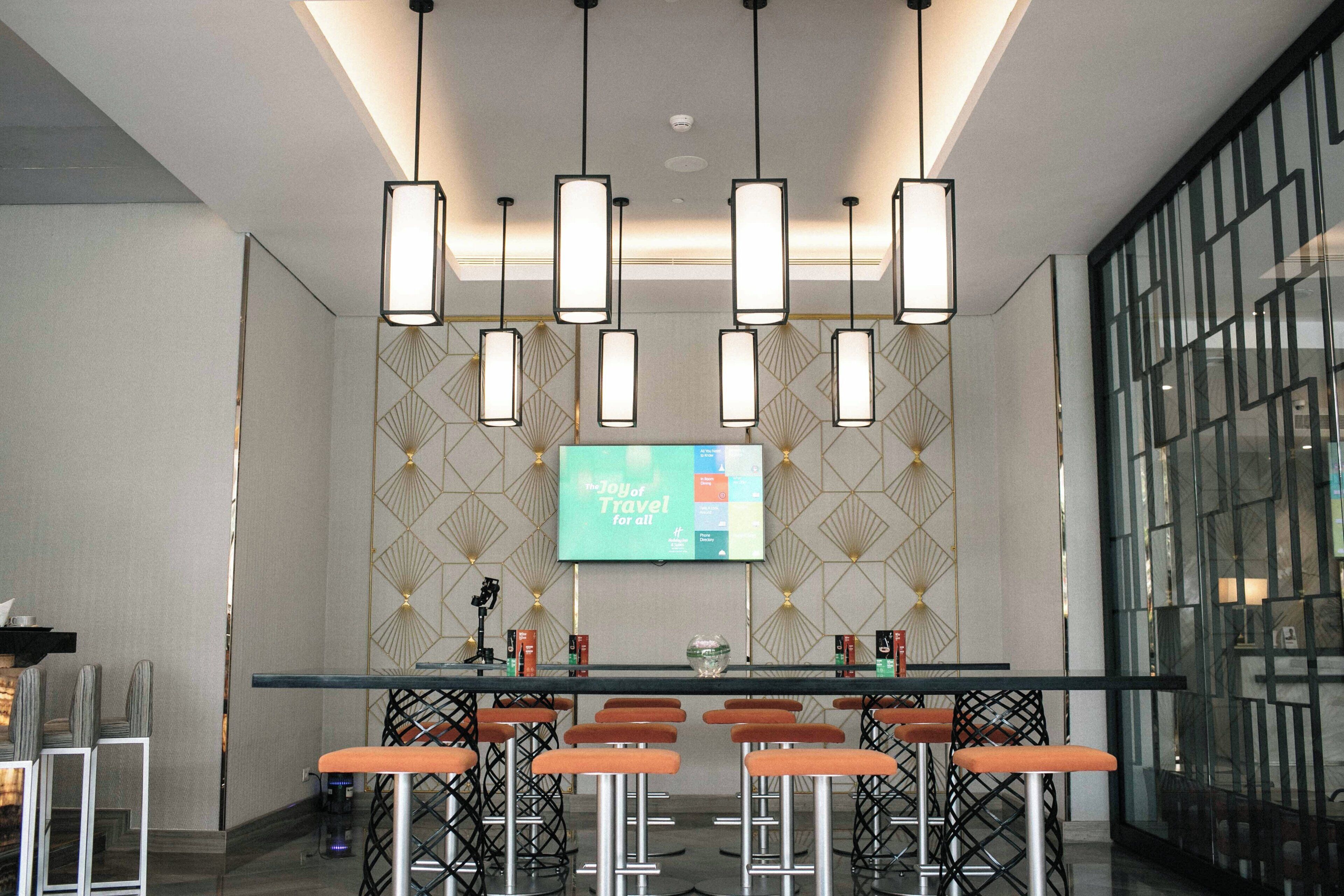 A bar area with multiple stools, a flat-screen TV mounted on the wall, and pendant lights.
