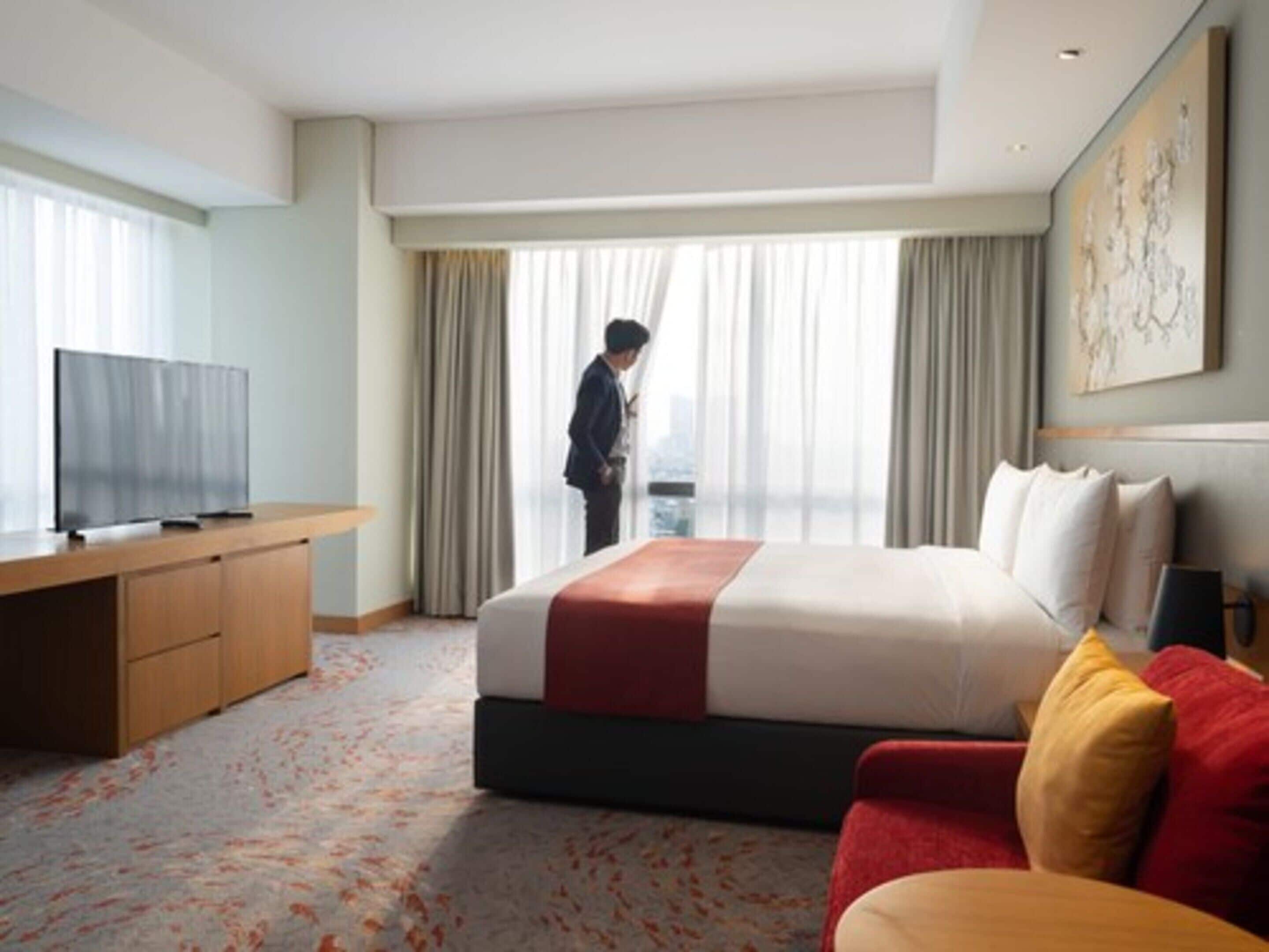 Une chambre d’hôtel avec un lit, une télévision, un bureau et une grande fenêtre avec des rideaux.
