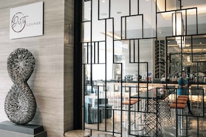 Un interior moderno con un separador de vidrio geométrico, una escultura abstracta única y una zona de bar visible con asientos.
