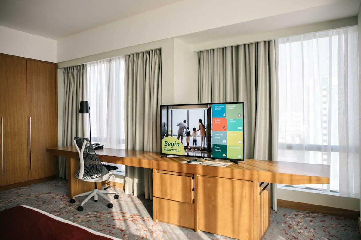 Een hotelkamer met een houten bureau, een stoel, een flatscreen televisie en een raam met gordijnen.