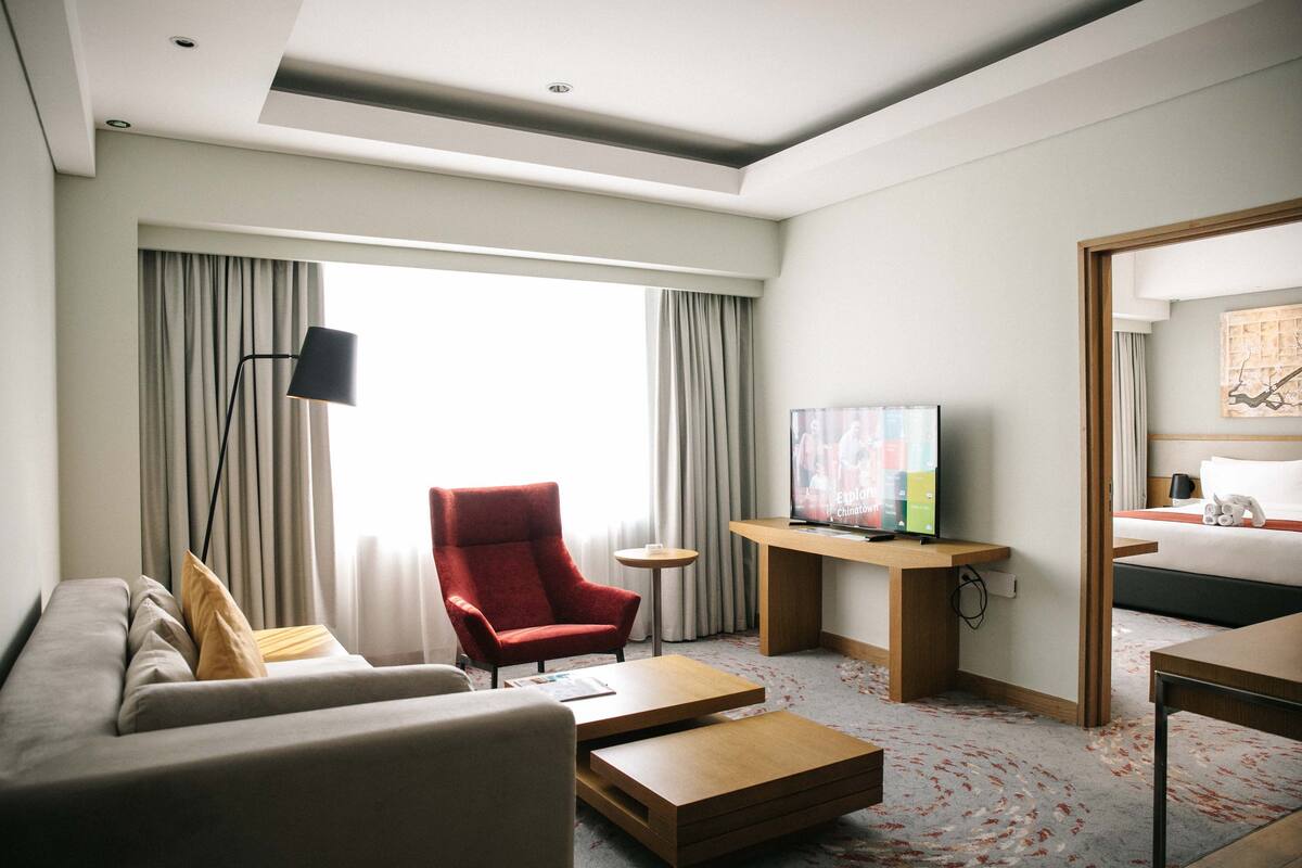 Een hotelkamer met een bank, een rode fauteuil, een televisie, een bed en een bureau.