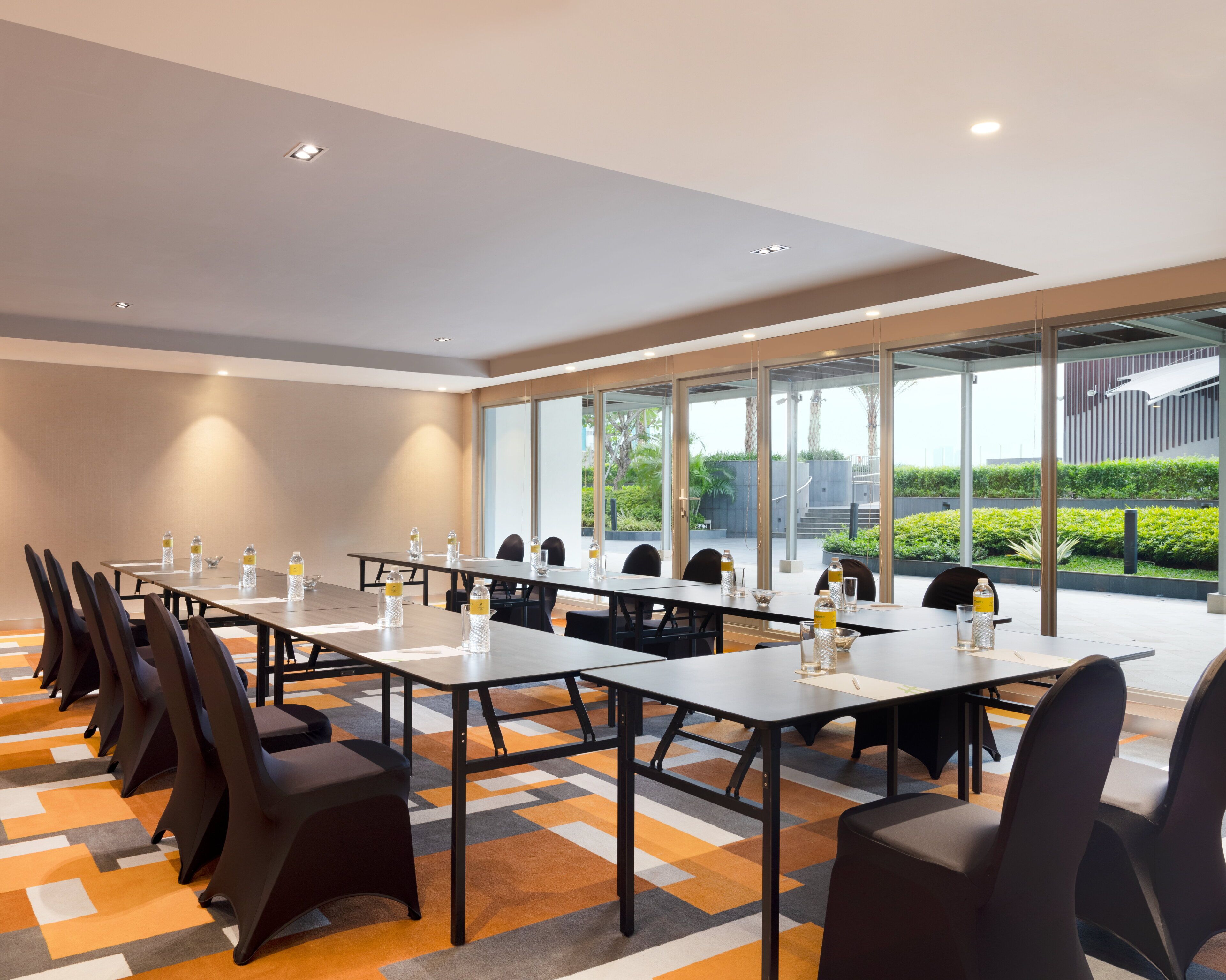 A conference room with long tables, chairs, and a view of greenery outside.