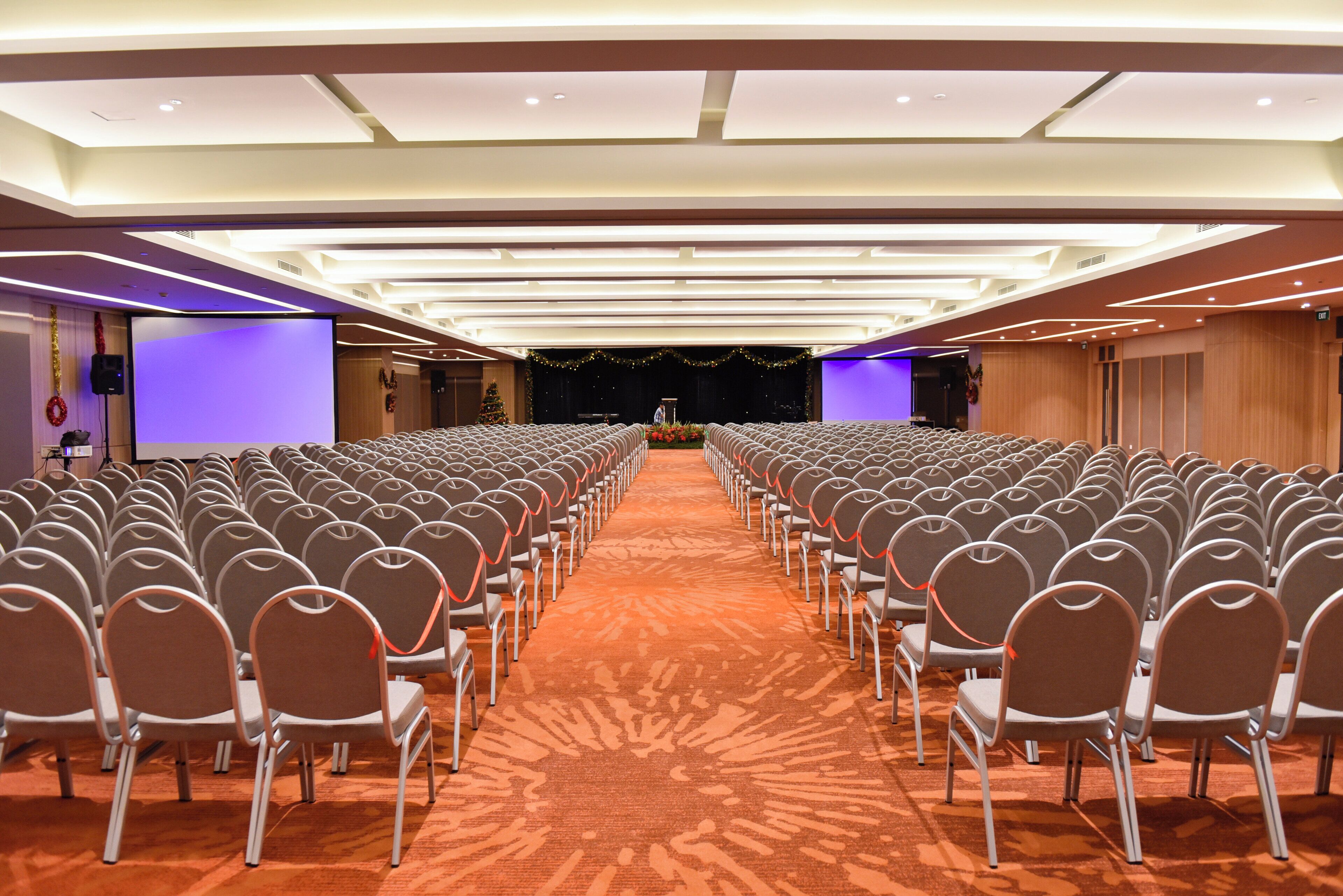 Een congreszaal met rijen stoelen gericht op een podium, voorzien van een projectiescherm en een geluidsinstallatie.