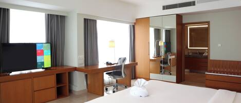 Une chambre d’hôtel avec un grand lit, un bureau avec une chaise, une télévision et une salle de bain visible à travers une porte en verre.