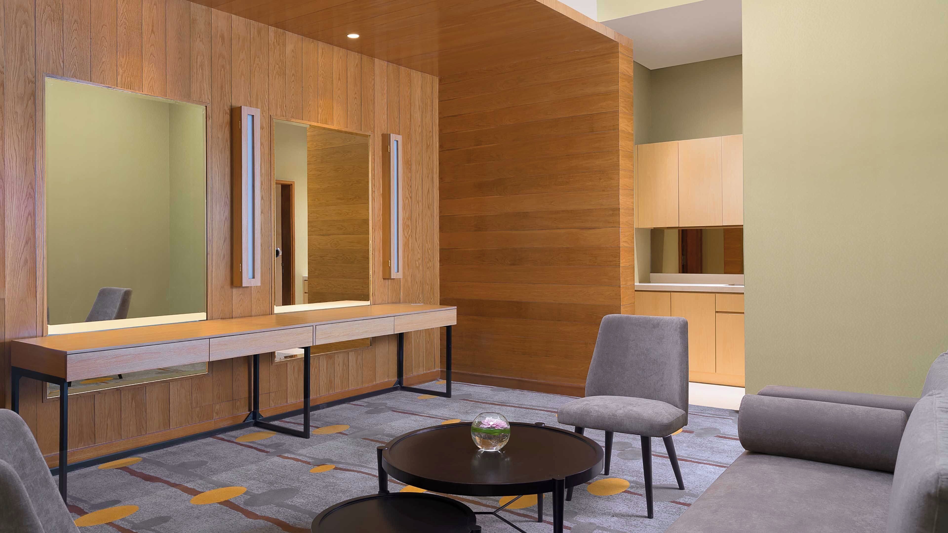 Ein modernes Hotelzimmer mit einem hölzernen Schminktisch, einem runden Couchtisch und einer Sitzecke mit Sofa und Sesseln.