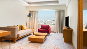 Una habitación de hotel moderna con vista a la ciudad, un sofá, un sillón rojo, un televisor y un escritorio.