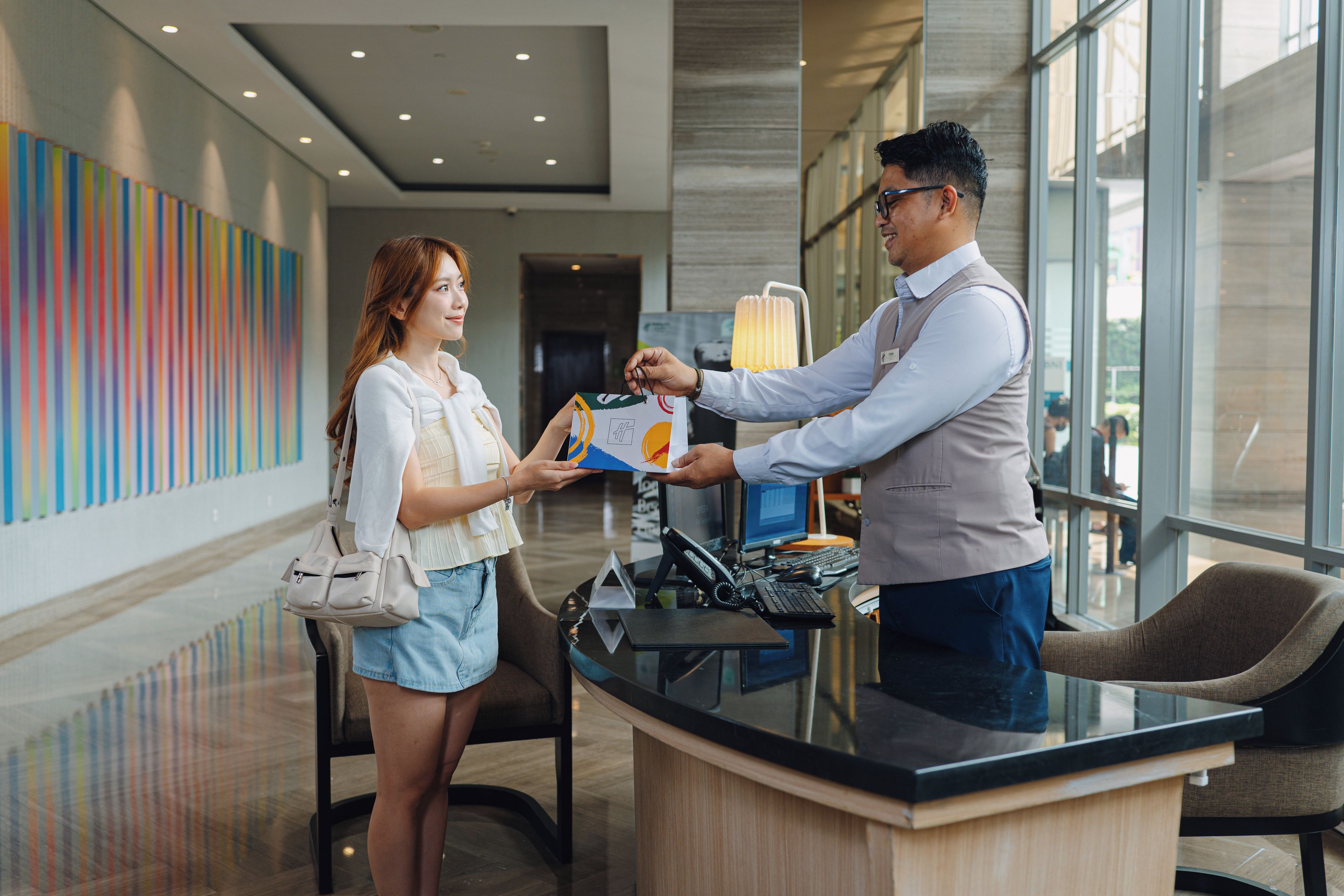 A hotel reception area with a modern interior, a reception desk, and a large window providing a view of the outside.