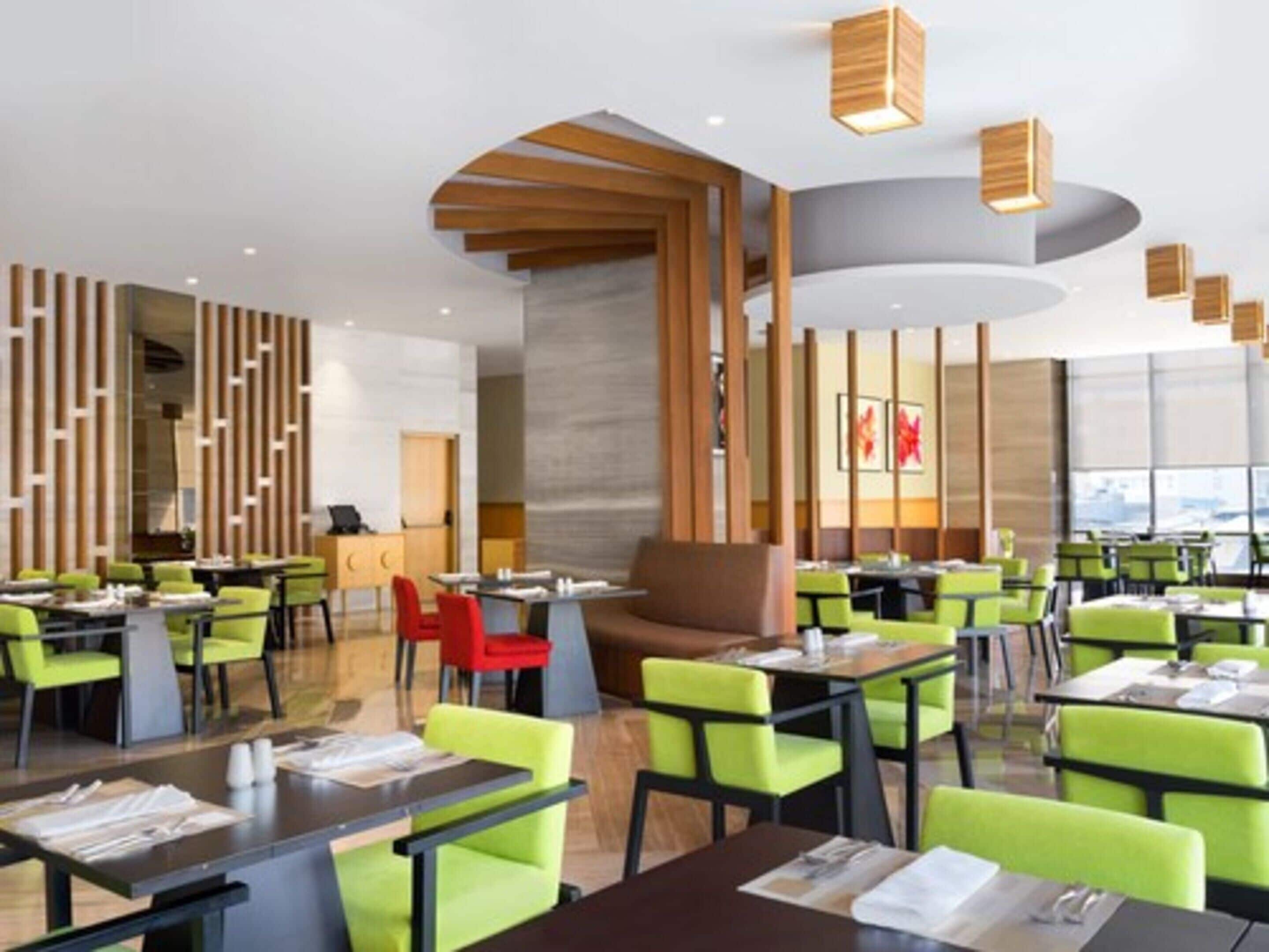 Un restaurante moderno con sillas verdes y rojas, detalles de madera y un diseño de techo curvo.