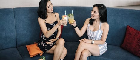 Two individuals seated on a sofa with drinks, a wallet, and a card on the table.