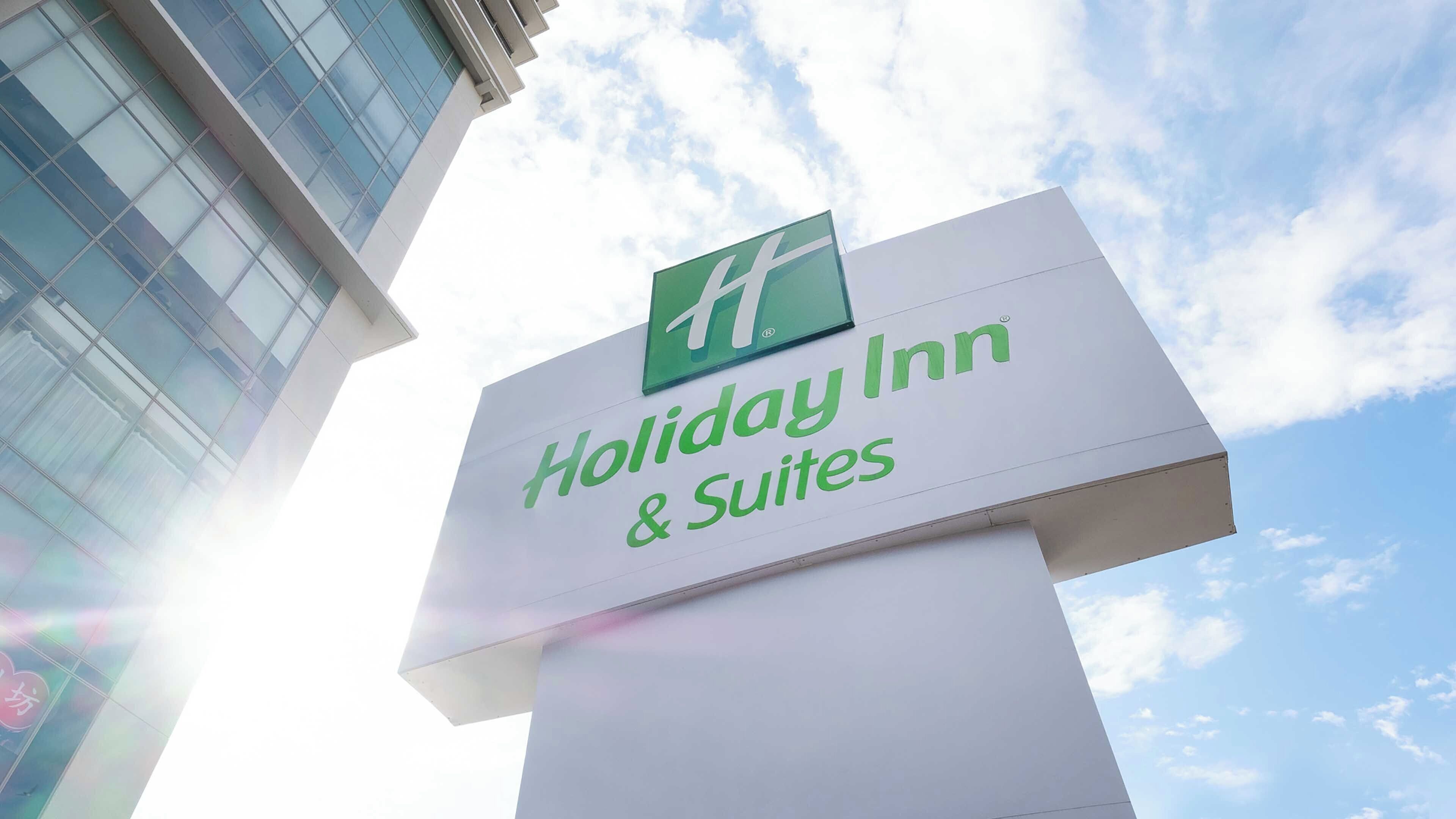 Schild für Holiday Inn & Suites mit einem modernen Gebäude im Hintergrund.