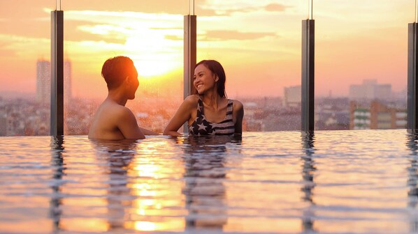 Una pareja en una piscina exterior climatizada, con un paisaje urbano al fondo.