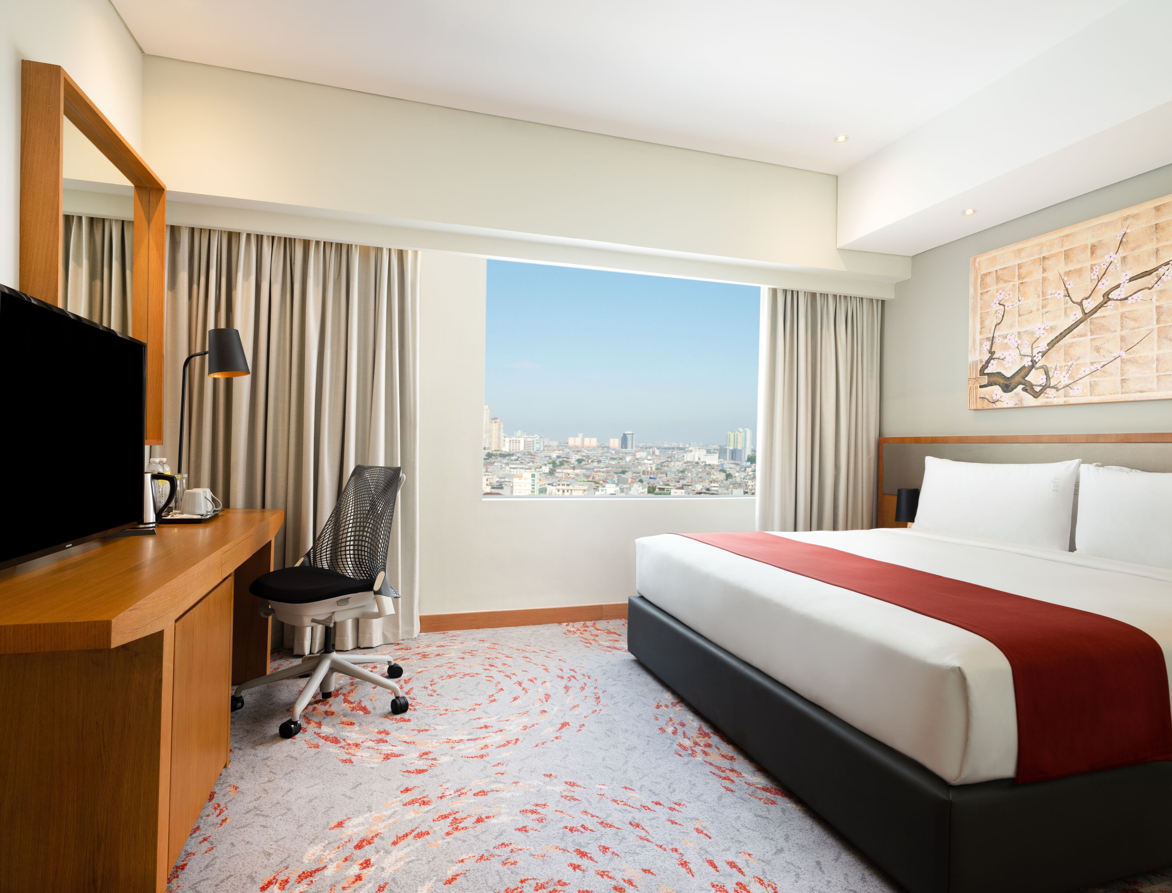 Une chambre d’hôtel comprenant un lit, un bureau avec une télévision, une chaise et une grande fenêtre donnant sur la ville.