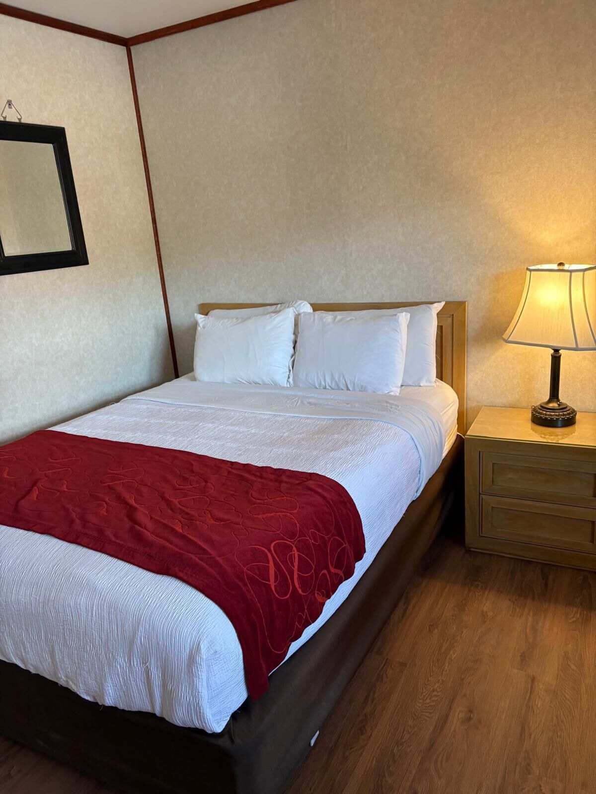 A hotel room with a bed, a nightstand, a lamp, and a wall-mounted mirror.
