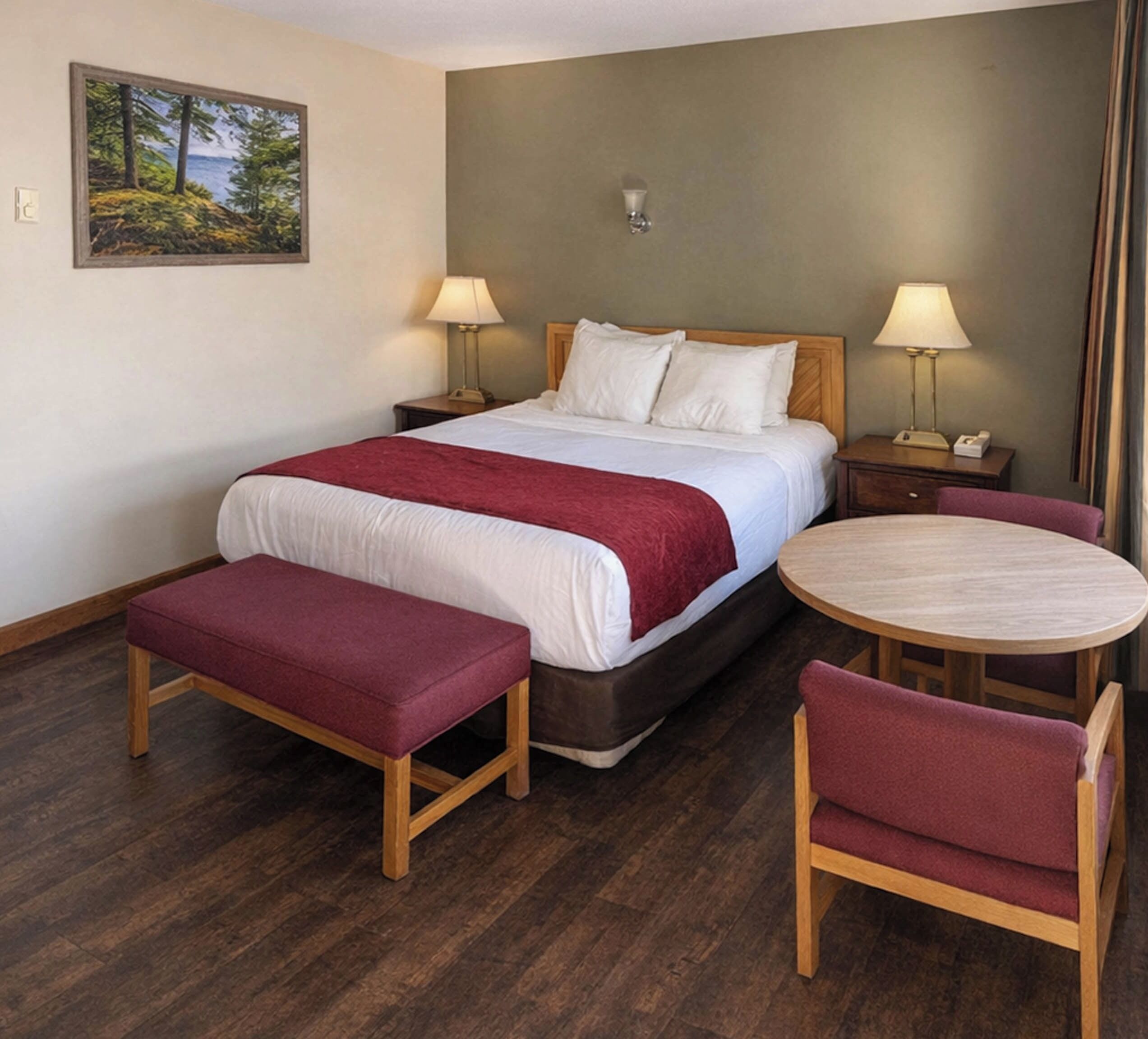 A hotel room with a bed, bedside lamps, a bench, a round table, and a chair.