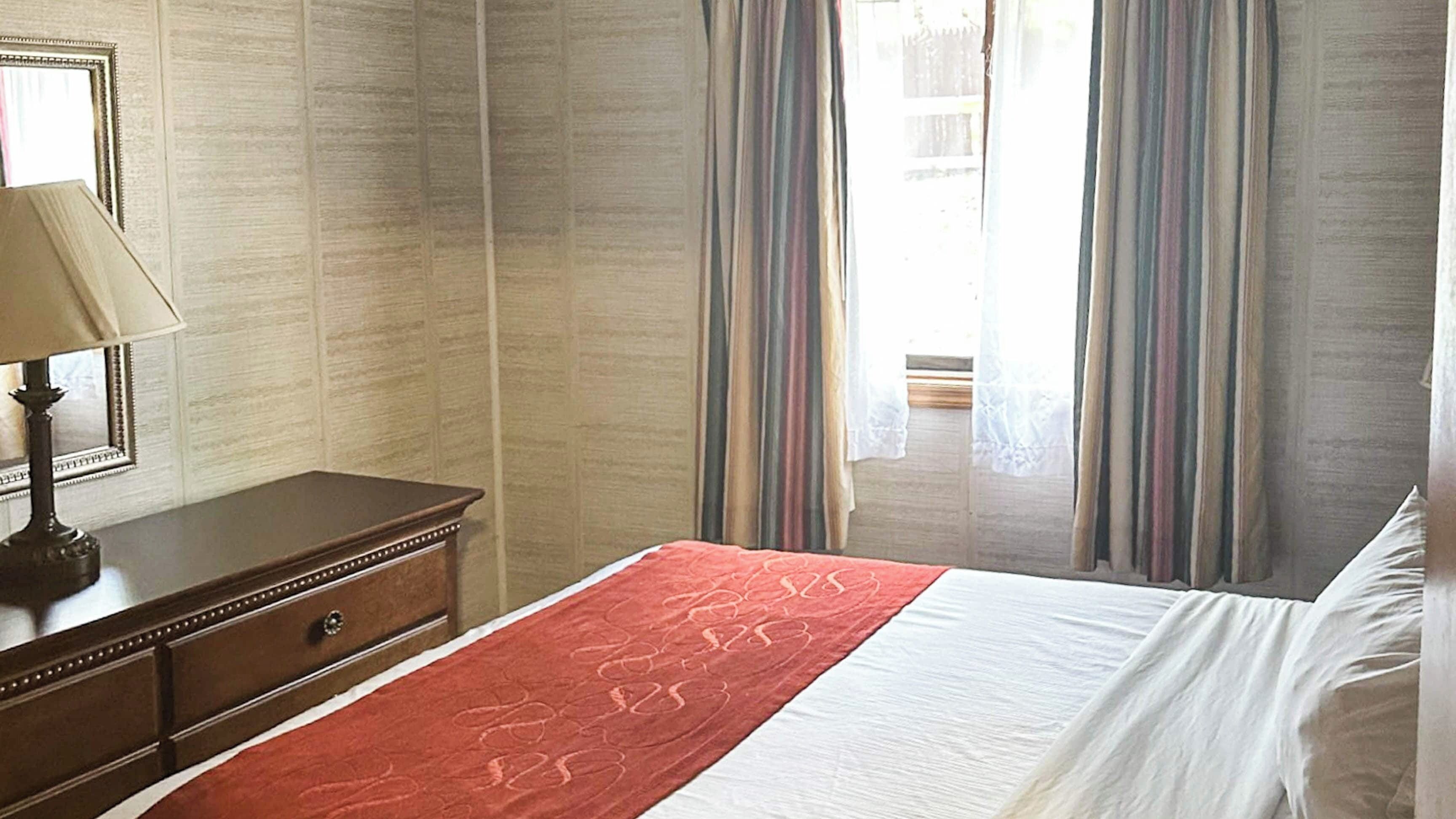 A hotel room with a bed, a nightstand, a lamp, and curtains.