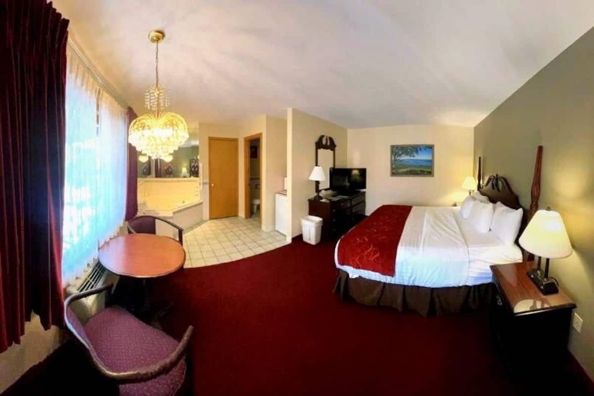 A hotel room with a bed, a desk, a chair, a TV, a lamp, and a window with curtains.