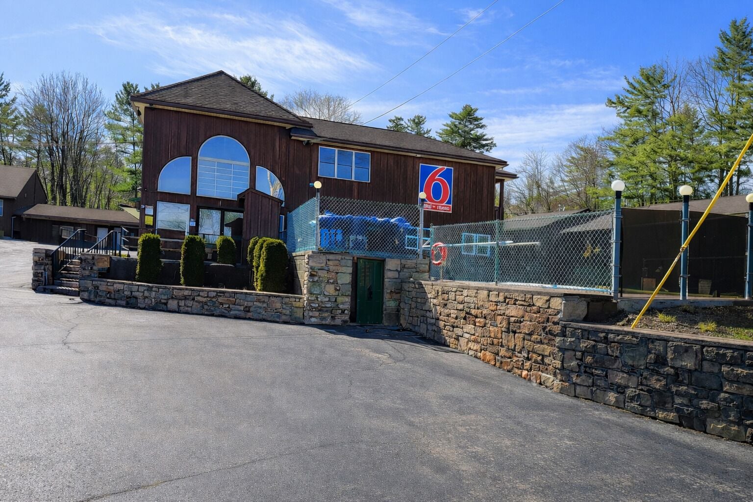 A two-story building with a large arched window, a sign with the number 6, and a stone wall in front.