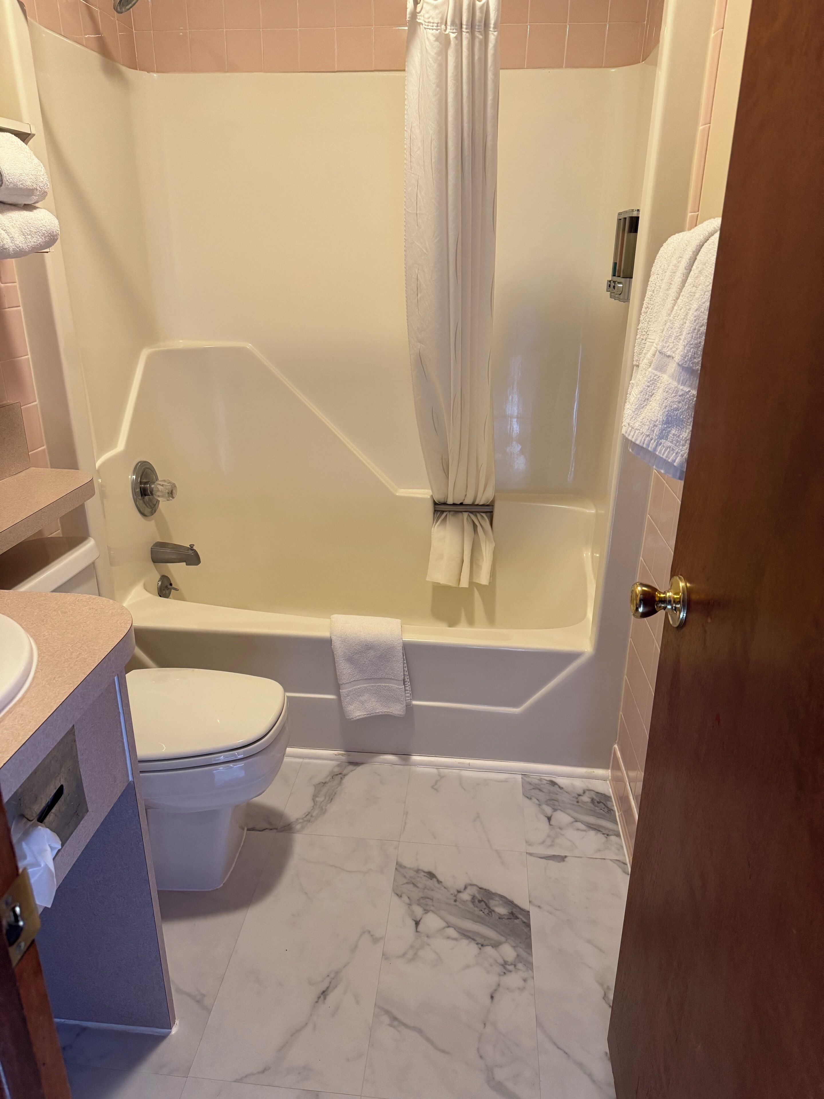 A bathroom with a bathtub, toilet, and marble floor.
