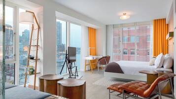 A modern hotel room with a large bed, a desk, a chair, and a view of the city.