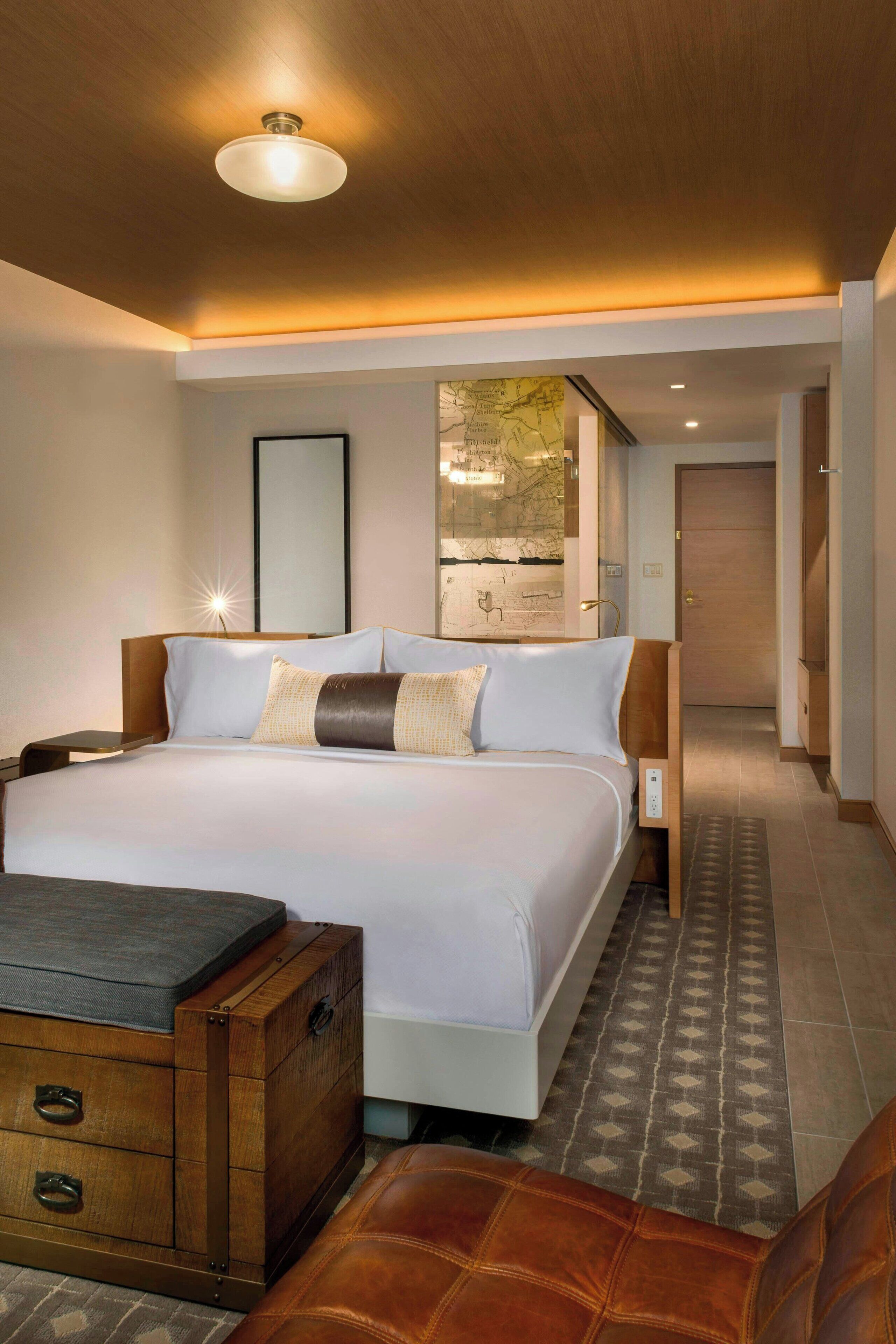 Una habitación de hotel con una cama grande, un aparador de madera, un reposapiés de cuero y un mapa en la pared.