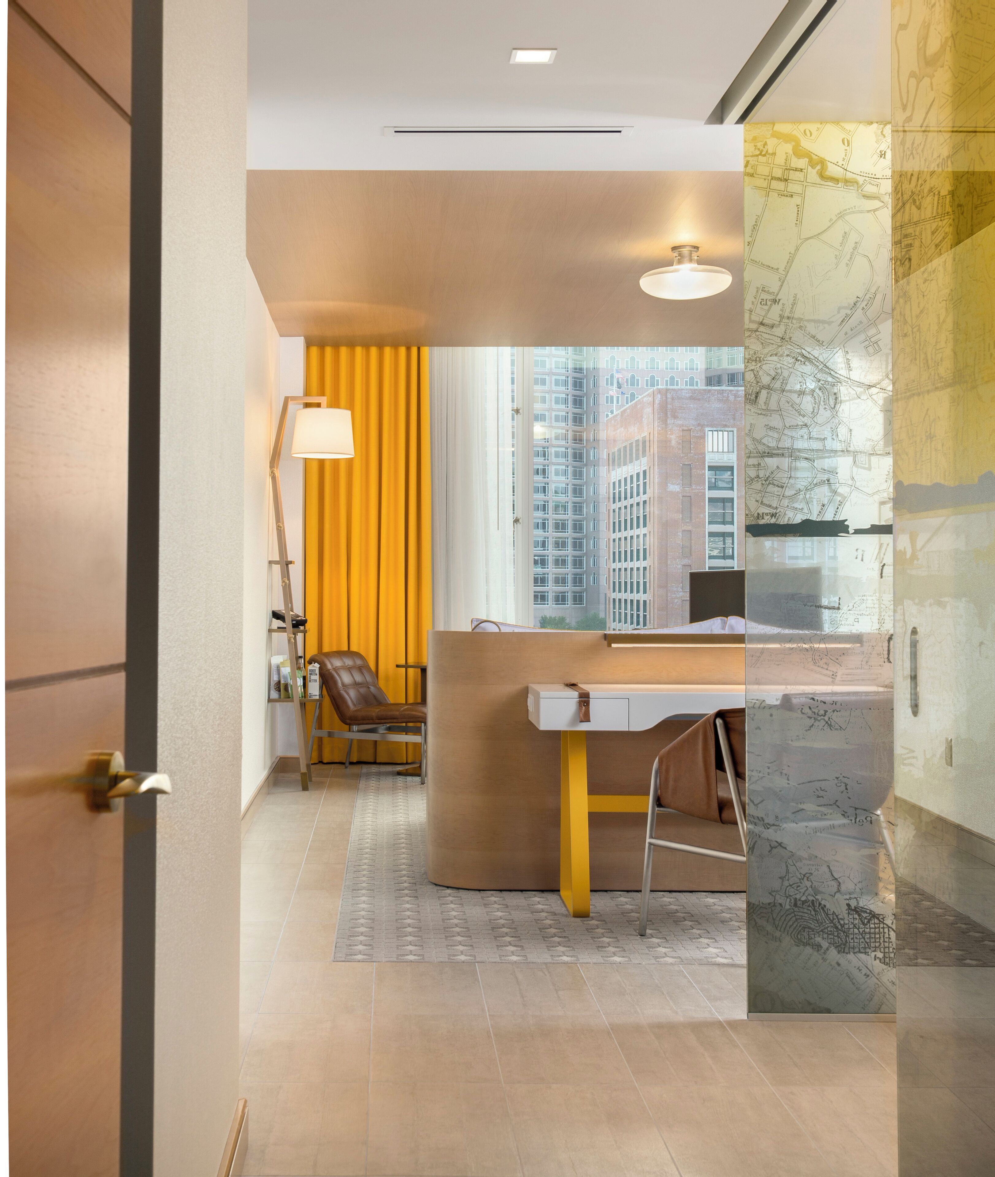 Une chambre d’hôtel moderne dotée d’une grande fenêtre, d’un bureau, d’une chaise et d’une lampe.
