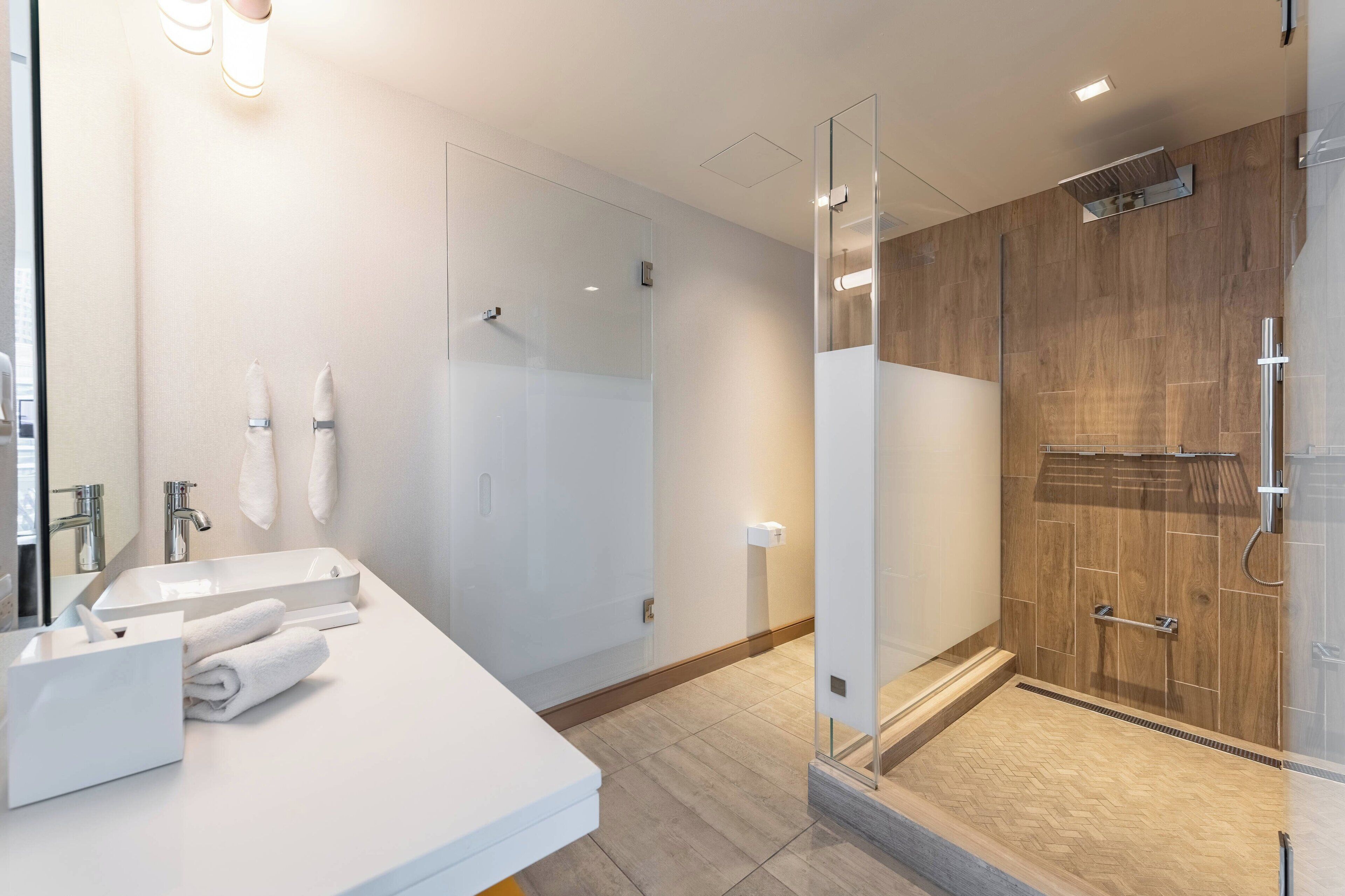 A modern bathroom with a glass shower enclosure, a white sink with a mirror, and a wooden shower area.