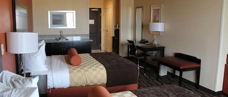 A hotel room with a bed, a desk, a chair, a bathroom, and a view of the outside.