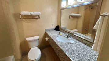 A bathroom with a toilet, sink, and mirror. There are towels on the wall and a bag on the counter.