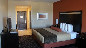 Quarto de hotel com cama, escrivaninha, televisão e porta de acesso a outro espaço.