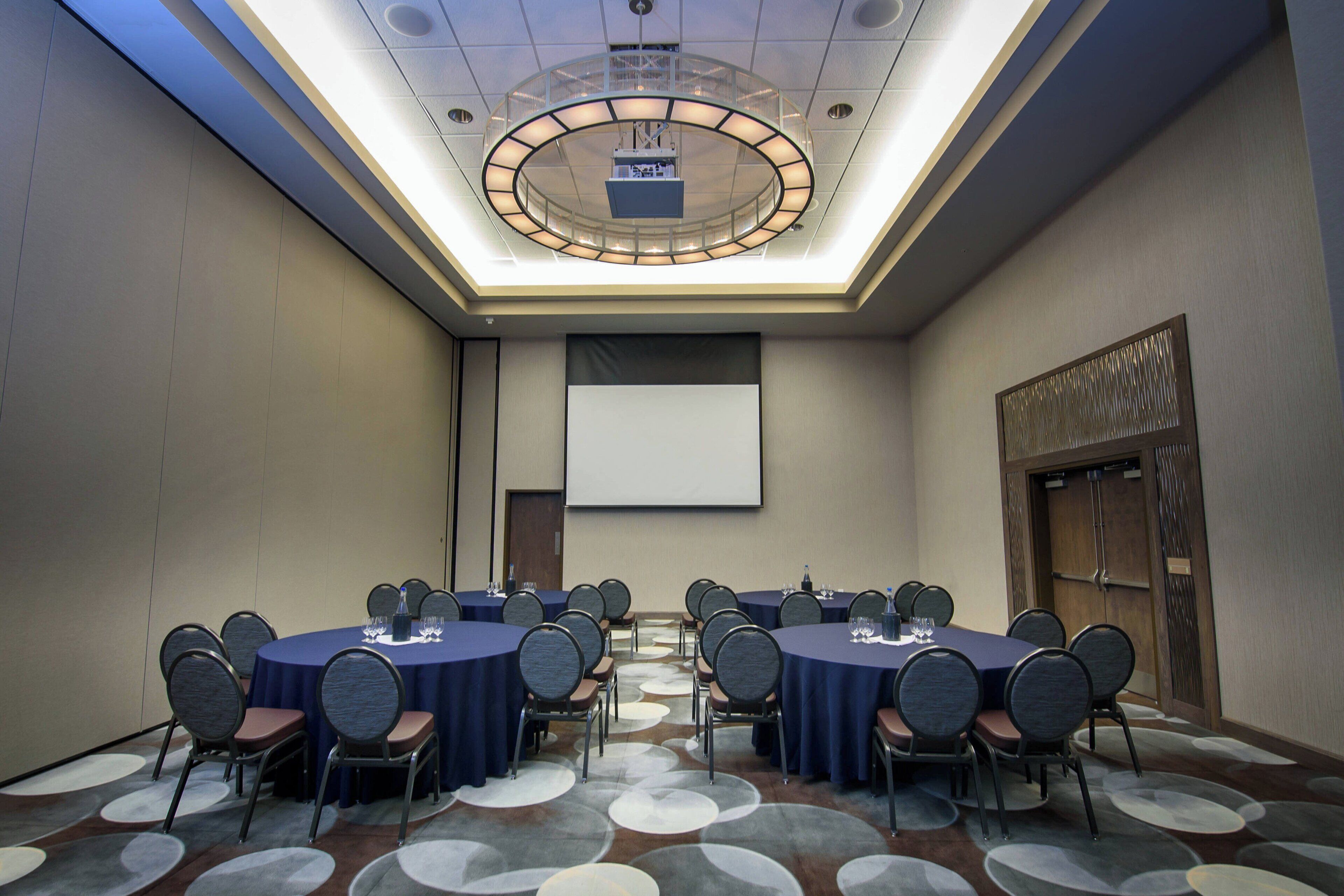 A conference room with a large table, chairs, a projector screen, and a ceiling light fixture.