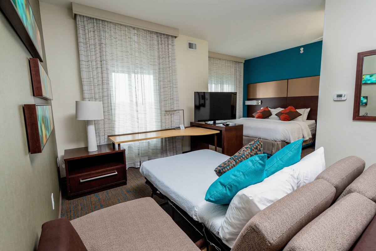 A hotel room with a bed, a desk, a TV, and a large window with curtains.