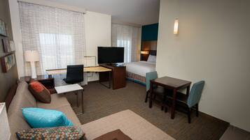 A hotel room with a bed, a desk, a chair, a sofa, and a television.