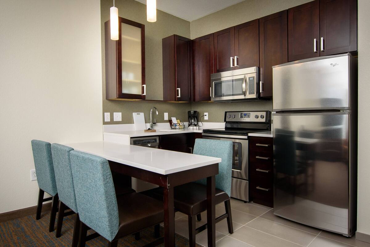 A modern kitchen with dark wooden cabinets, stainless steel appliances, and teal upholstered chairs.