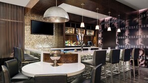 Zona de bar moderna con una mesa redonda, taburetes, un televisor de pantalla plana y una variedad de botellas en estanterías.
